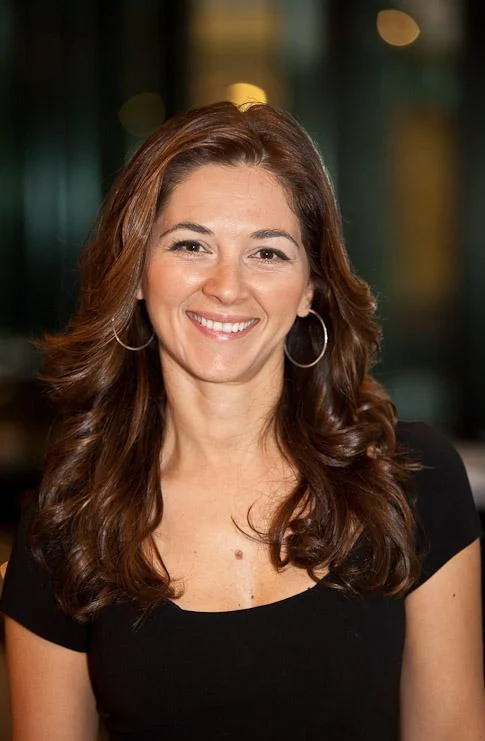 Ani Wenger smiling, with long auburn waves, in a black top
