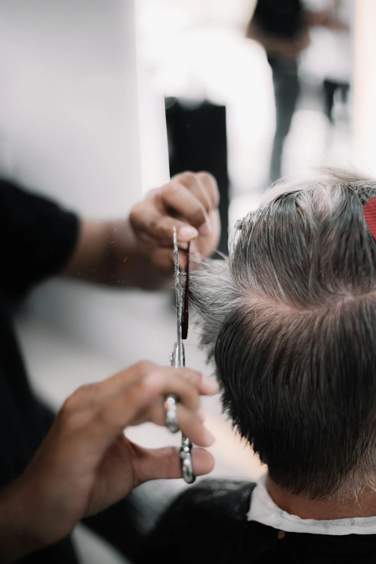 A scissor and comb cut on a man's salt-and-pepper hair, seen from behind