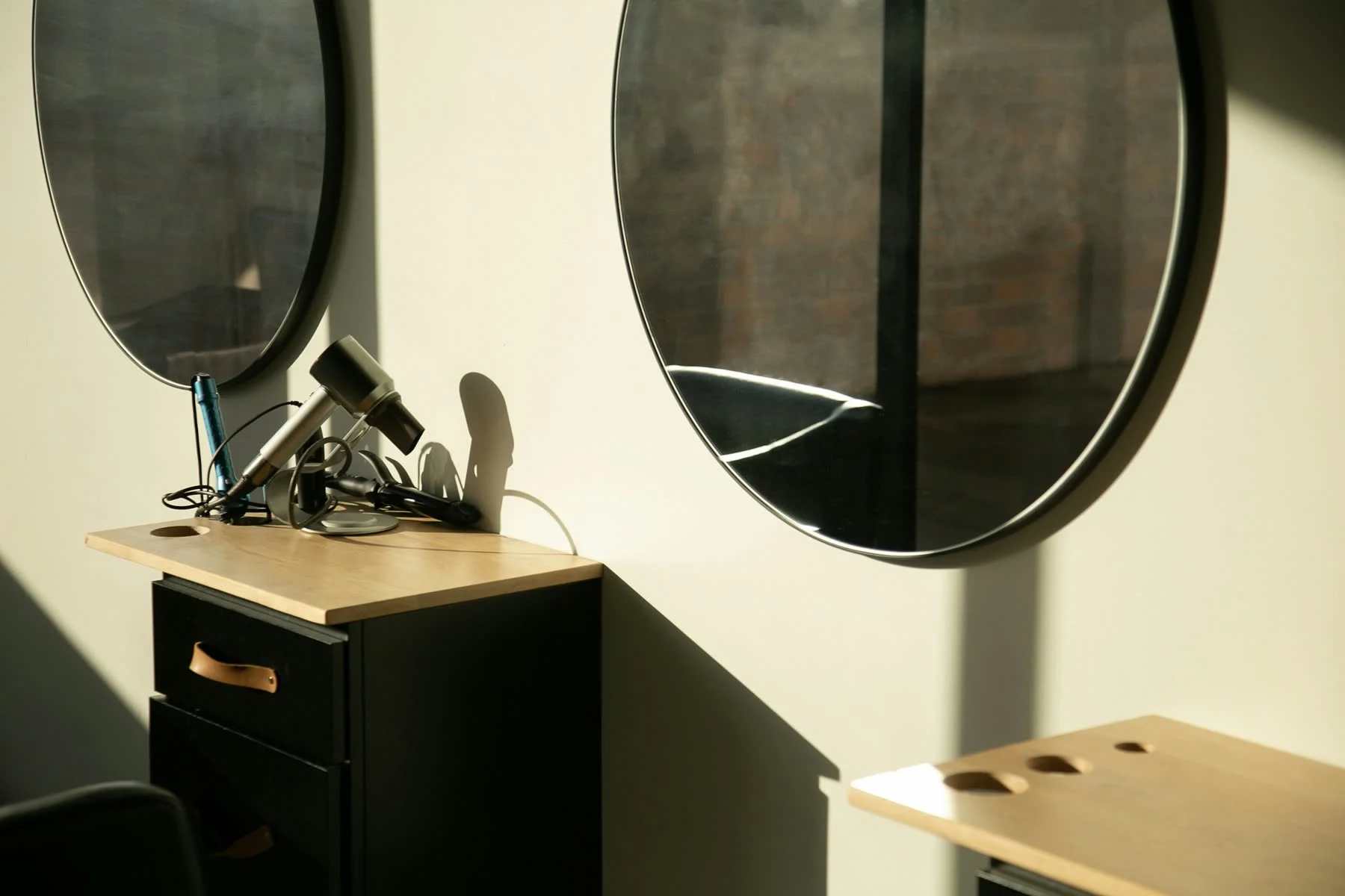 Warm afternoon light across a minimal styling station with round mirrors and a pale wood counter