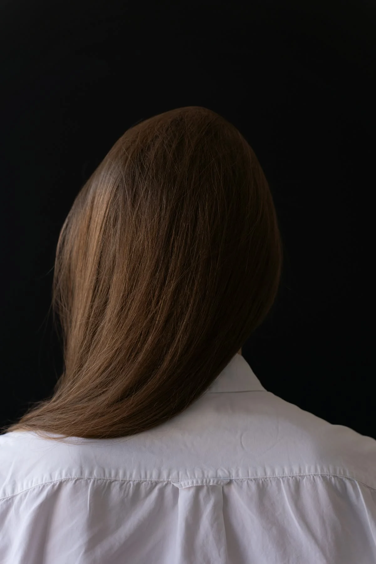 Sleek, frizz-free brown hair over the shoulders of a white shirt, seen from behind