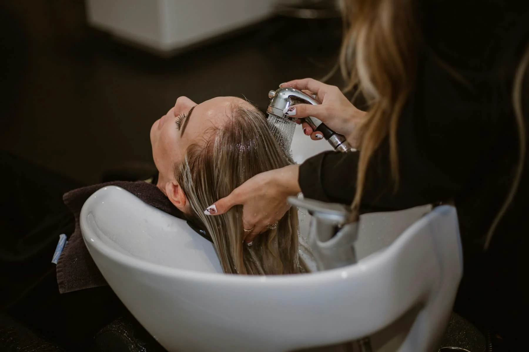A client's long hair being rinsed at a white salon basin during a treatment