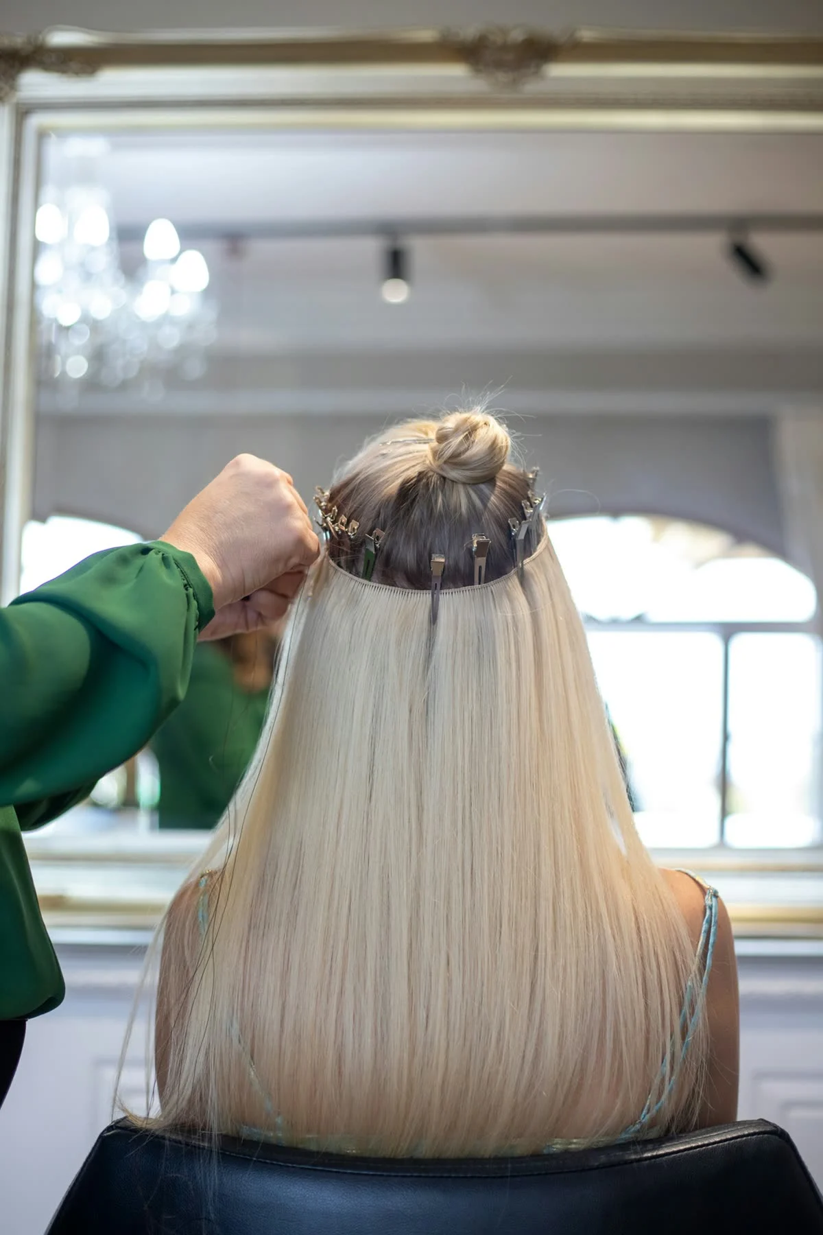 A stylist fits extension wefts into long platinum hair in front of a gilded mirror