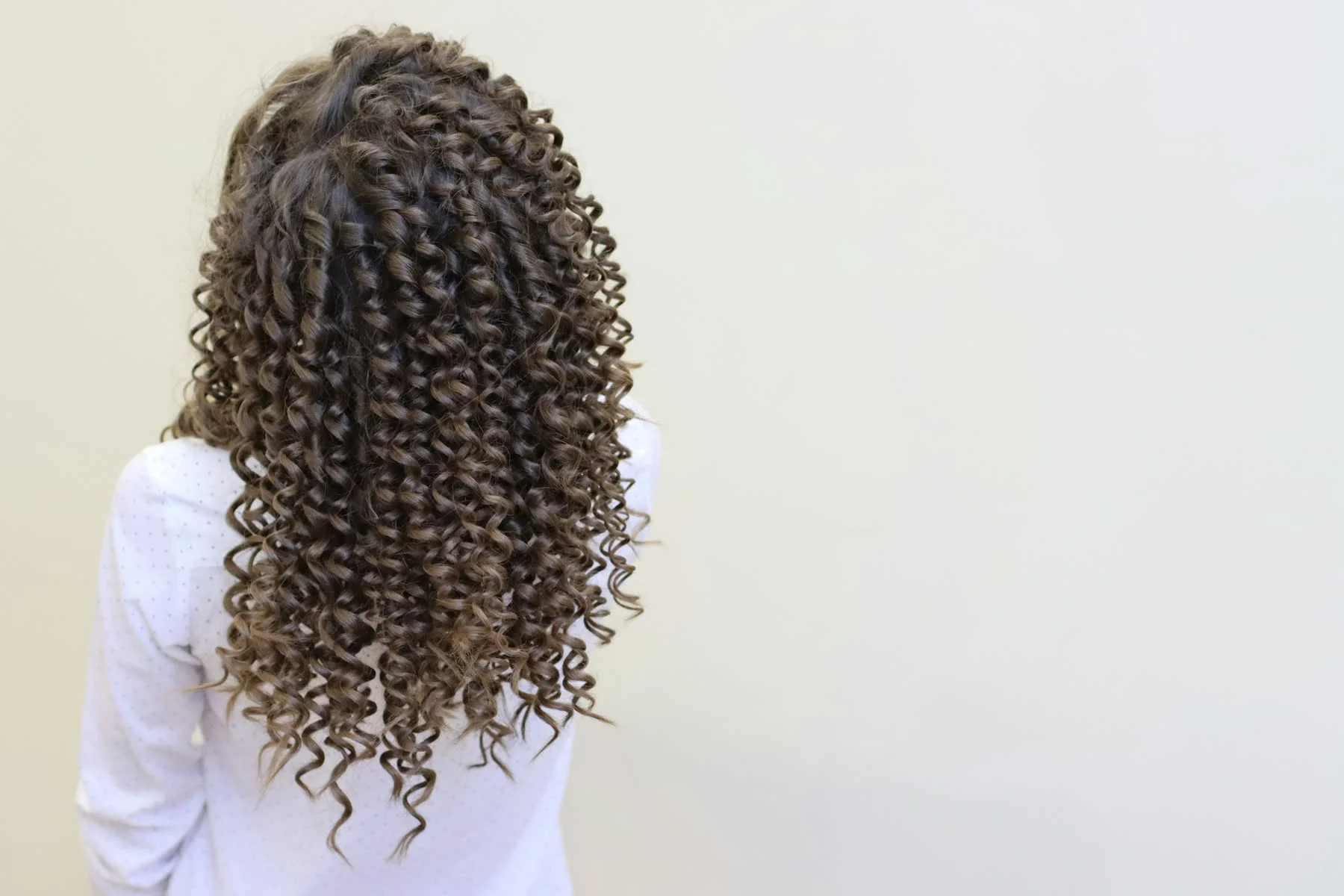 Long, defined spiral curls seen from behind against a cream wall